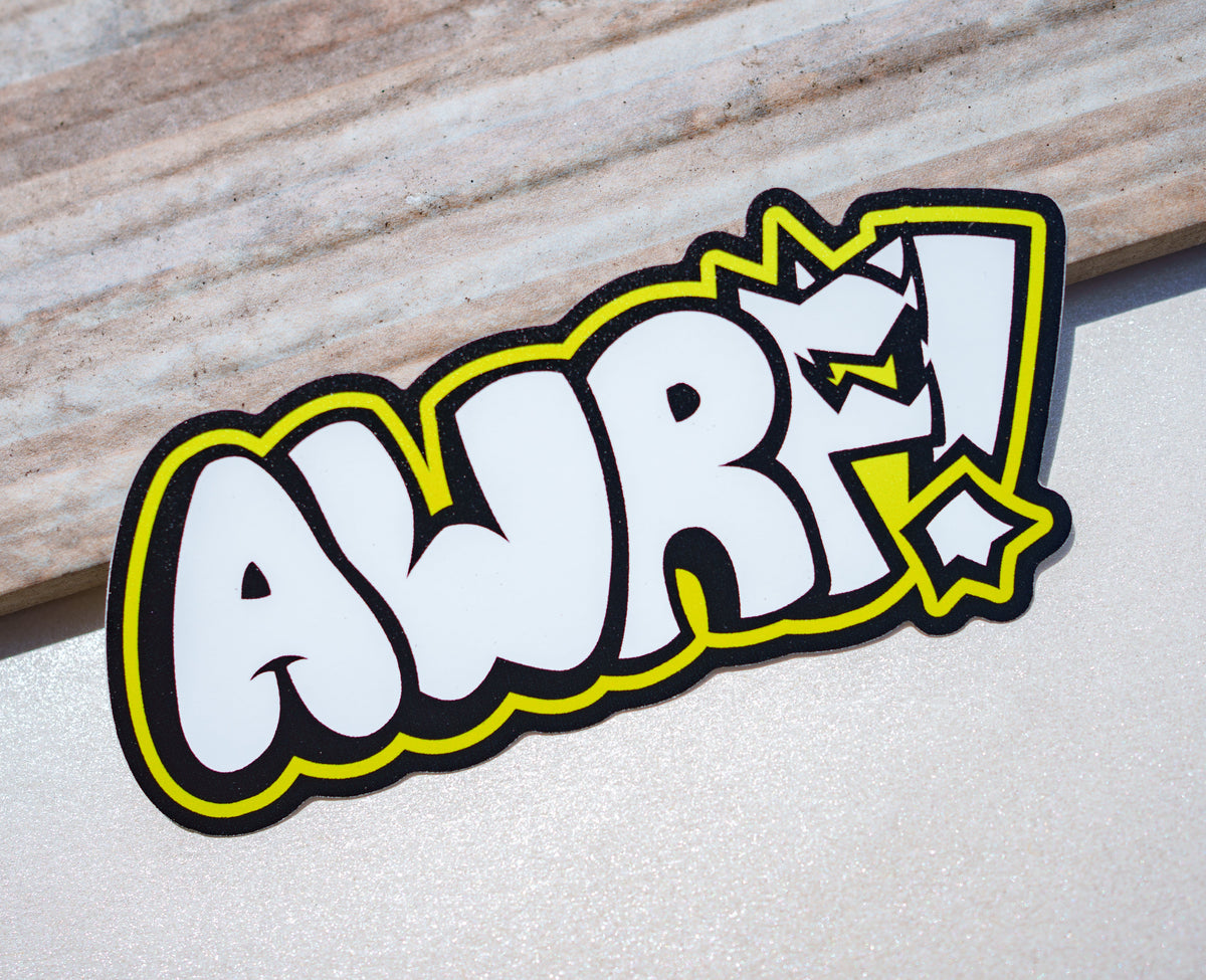 A die-cut sticker featuring the word 'AWRF!' in a bold white comic-style font with a black outline and bright yellow border, placed on a light surface with a wood-grain board in the background.